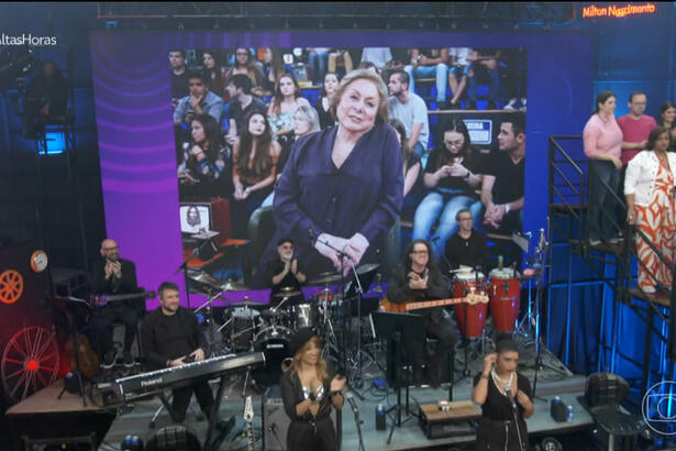 Telão mostrando imagem de Aracy Balabanian de camisa roxa, sentada, durante entrevista no programa Altas Horas, da TV Globo