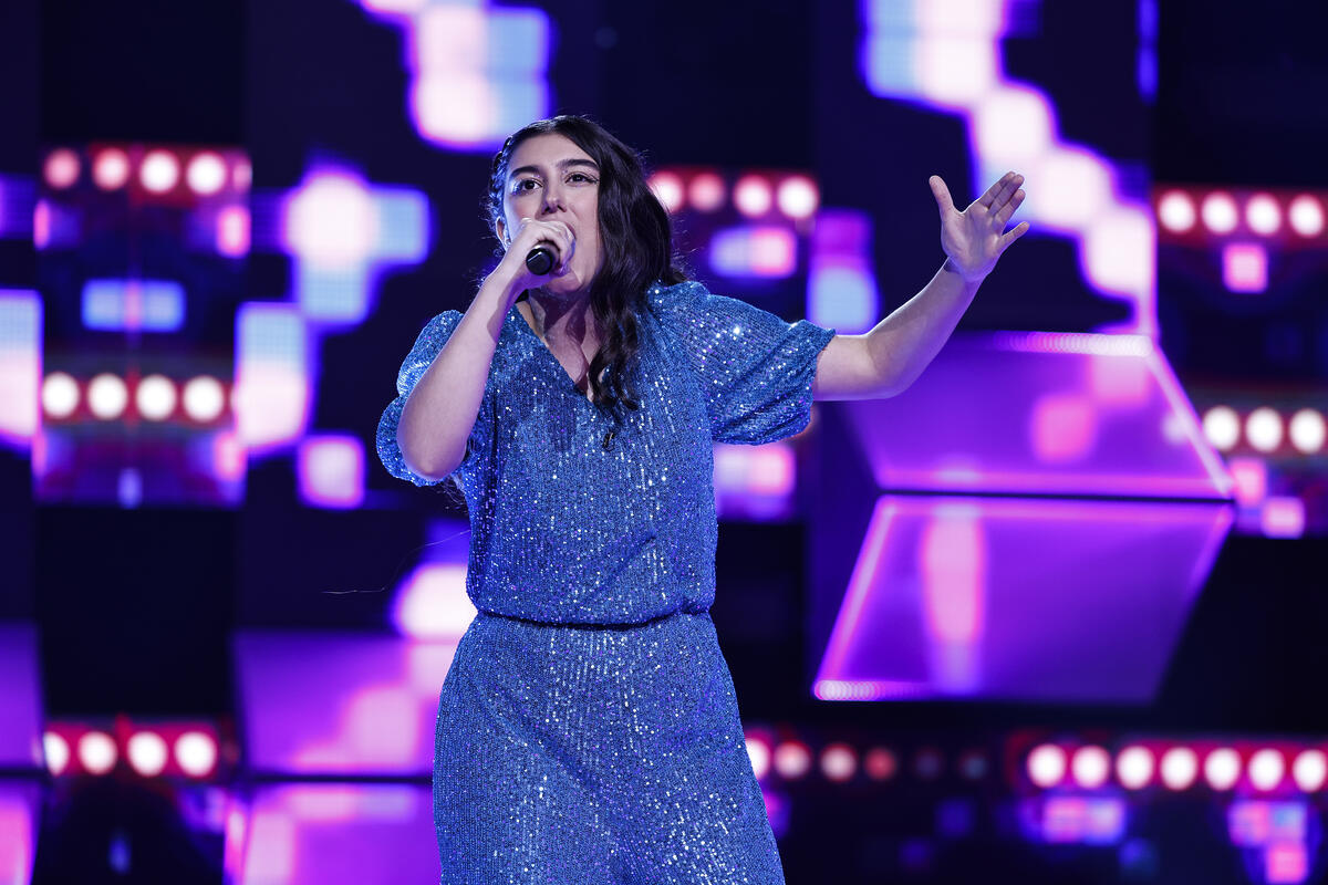 Natália Calanga se apresenta no palco do Canta Comigo Teen 4. Ela veste um macacão azul cheio de brilho.