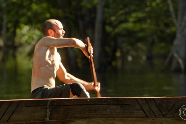 Dedé sem camisa, segurando o remo, remando no barco durante prova do No Limite 2023