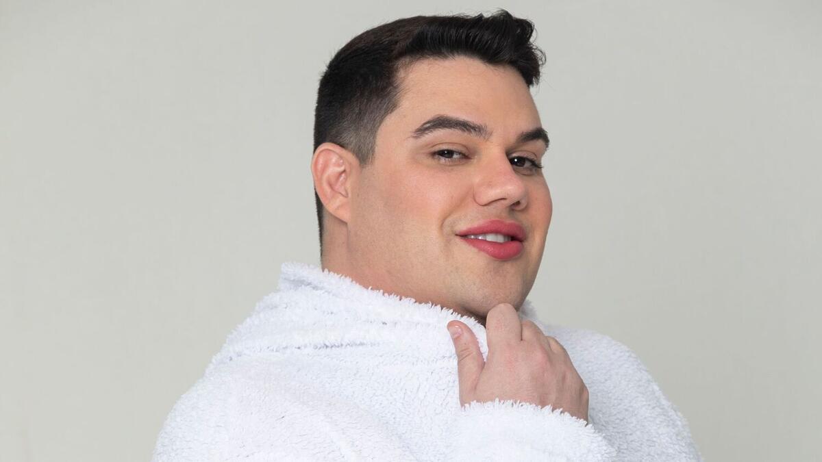 Erick Ricarte sorrindo, de camisa branca, com a mão no queixa