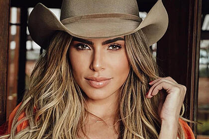 Erika schneider de chapéu de cowboy marrom, usando top laranja, cabelo solto durante ensaio fotográfico