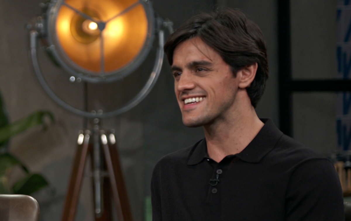 Felipe Simas sorrindo, de camisa preta, sentado em frente a Pedro Bial durante entrevista
