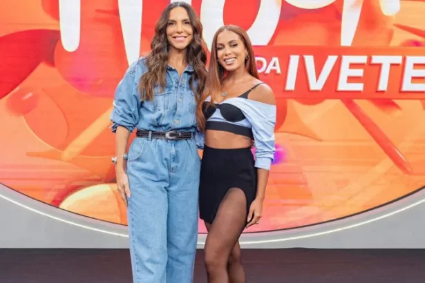 Ivete Sangalo vestindo total jeans azul, sorrindo, ao lado de Anitta, nos Estúdios Globo, para o Pipoca da Ivete