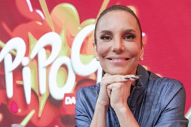 Ivete Sangalo sorrindo, de look total jeans, com as mãos juntas encostada no queixo cair