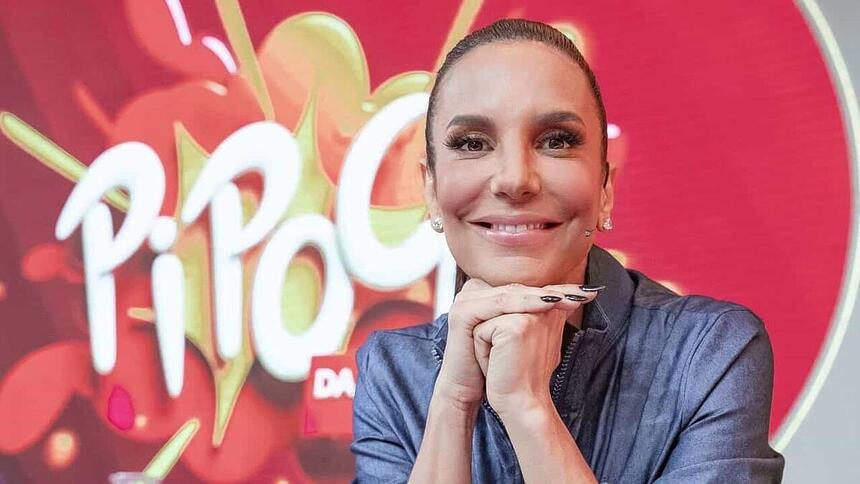 Ivete Sangalo sorrindo, de look total jeans, com as mãos juntas encostada no queixo cair