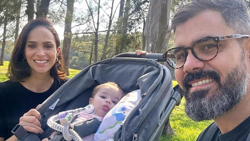 Juliano Cazarré e Leticia Cazarré em foto posada ao lado da filha, no carrinho e com o tubo de traqueostomia