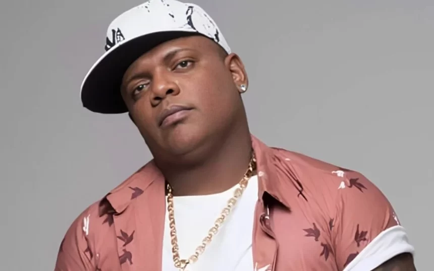 MC Marcinho de camisa rosa e branca, colar de brilhante dourado, chapéu branco durante ensaio fotográfico