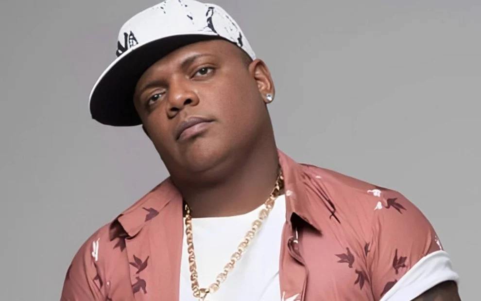 MC Marcinho de camisa rosa e branca, colar de brilhante dourado, chapéu branco durante ensaio fotográfico