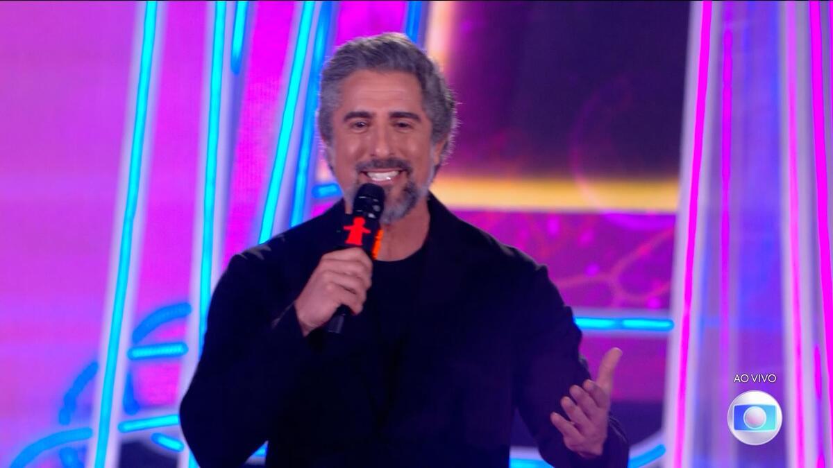 Marcos Mion sorrindo, de camisa preta, no palco do Criança Esperança
