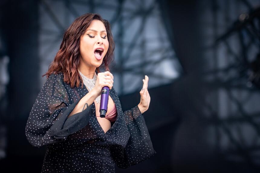 Pitty de boca aberta, segurando o microfone, usando um vestido decotado, cabelo solto durante performance em show