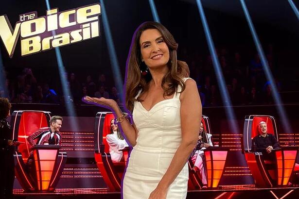 Fátima Bernardes de vestido branco, sorrindo, no estúdio do The Voice Brasil