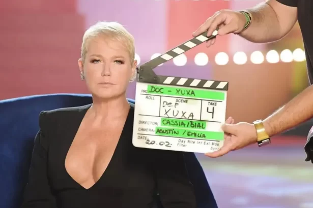 Xuxa de blaser preto, decotado, sentada durante gravação de documentário