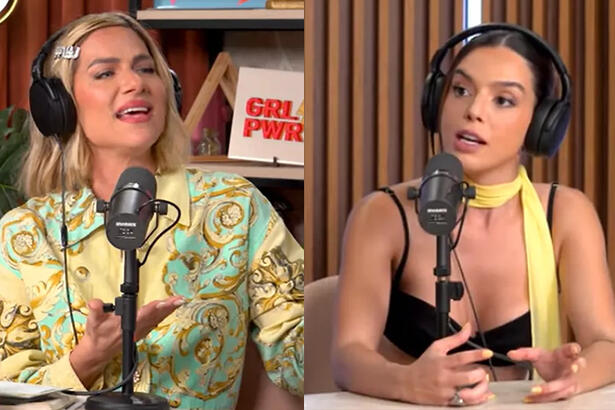 Giovanna Lancellotti de camisa preta e fone de ouvido, sentada durante entrevista com Giovanna Ewbank com camisa estampada em verde e amarela