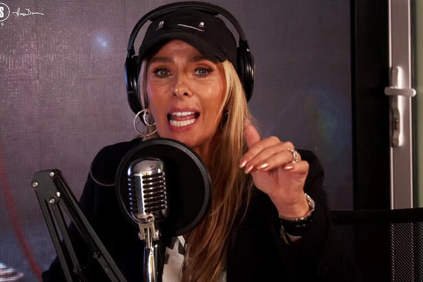 Adriane Galisteu de chapéu e camisa pretos, sentada, com fone de ouvido, durante entrevista no Podcaras