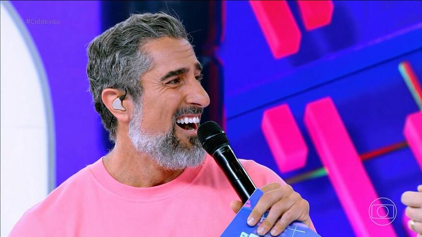 Marcos Mion de camisa rosa e sorrindo no Caldeirão