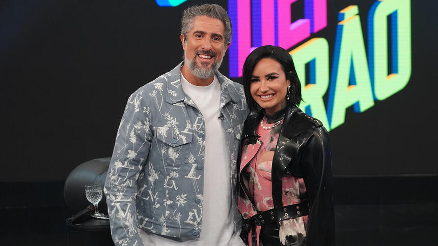 Demi Lovato e Marcos Mion posando abraçados nos bastidores do Caldeirão