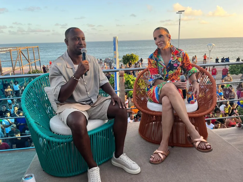 Ivete Sangalo sentada no banco ao lado de Thiaguinho, em cima de um trio elétrico durante gravação do Pipoca da Ivete