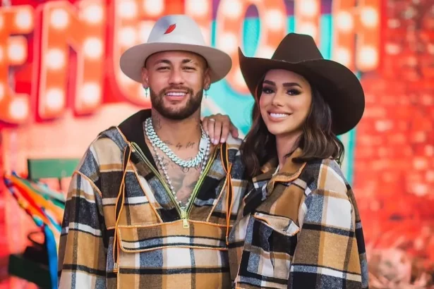 Neymar e Bruna Biancardi sorrindo, com camisa quadriculada, chapéu de cowboy, durante show