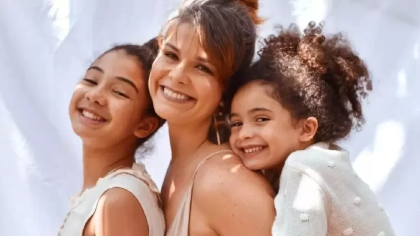 Samara Felippo sorrindo, de vestido bege, abraçada com as filhas em ensaio fotográfico