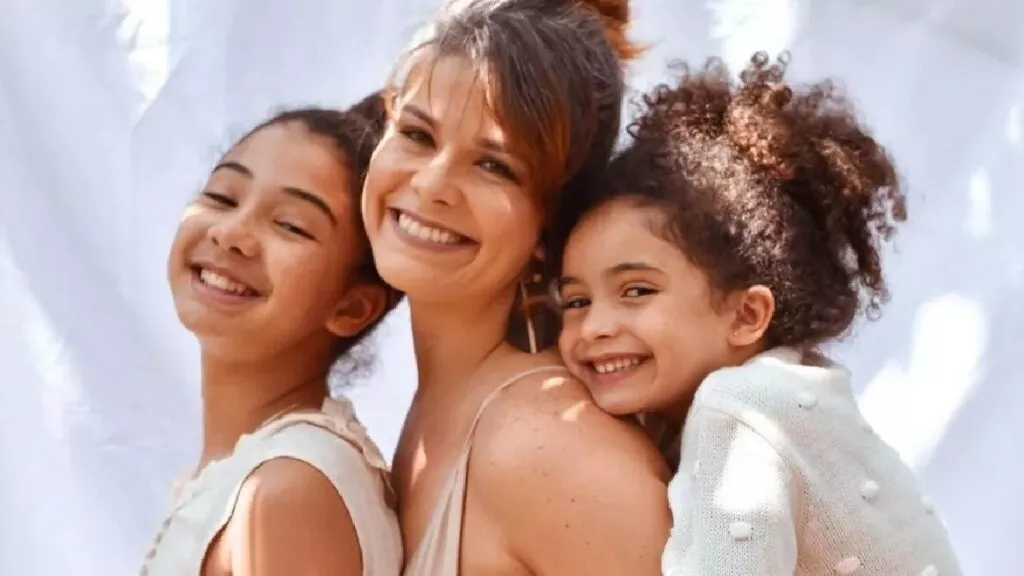 Samara Felippo sorrindo, de vestido bege, abraçada com as filhas em ensaio fotográfico