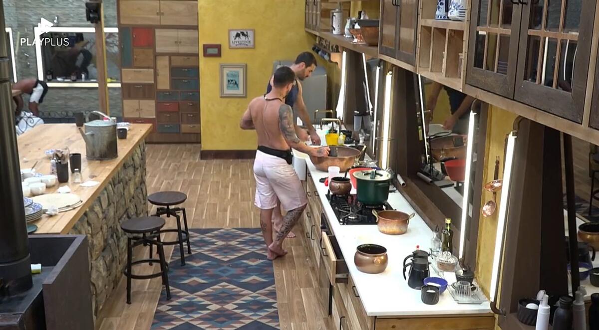 Shay e Radamés em pé na cozinha lavando a louça.