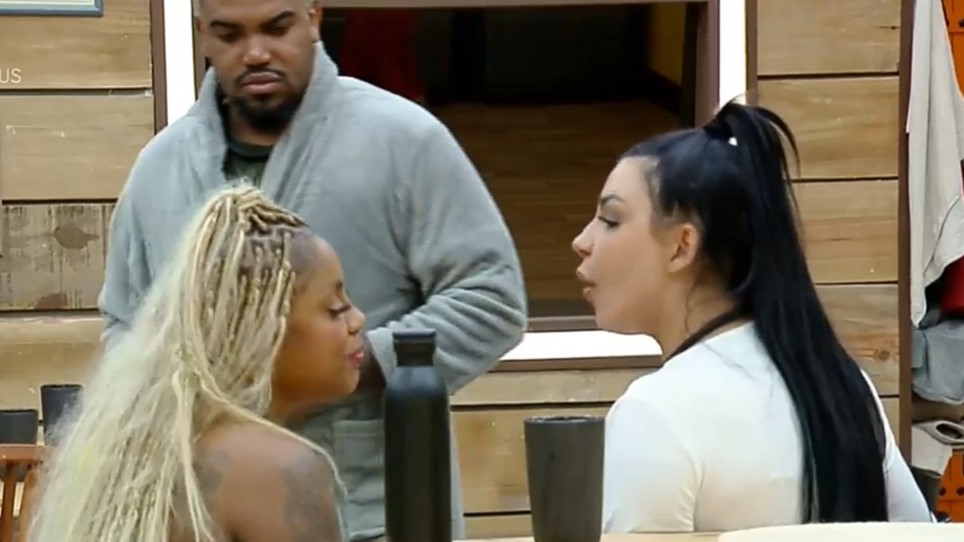 Caríucha sentada em frente a Jenny Miranda sorrindo dela na cozinha de A Fazenda