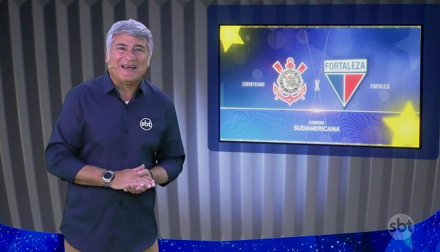 Cleber Machado no estúdio da Copa Sul Americana, na frente de uma tela com o logo do Corinthians e Fortaleza