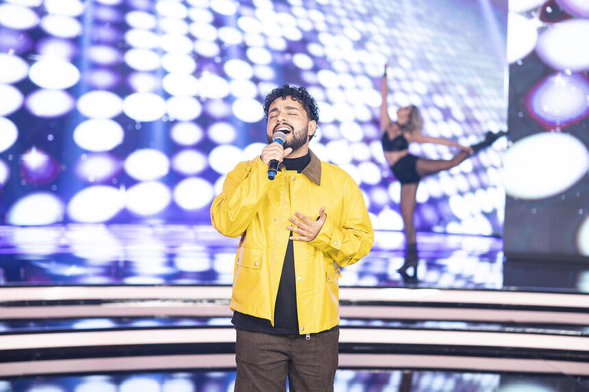 Gabriel Henrique de jaqueta amarela canta no palco do Hora do Faro