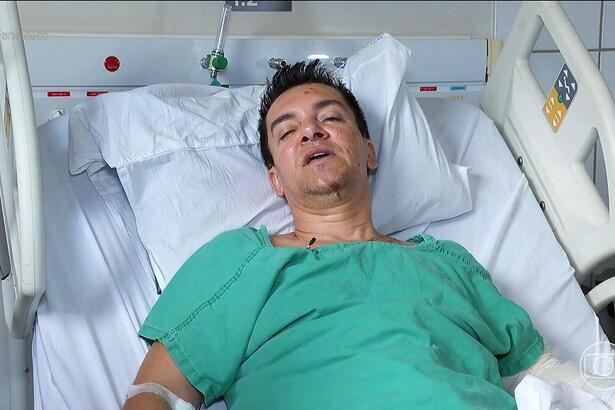 Regis Danese com roupa de hospital verde deitado na cama do HUGOL