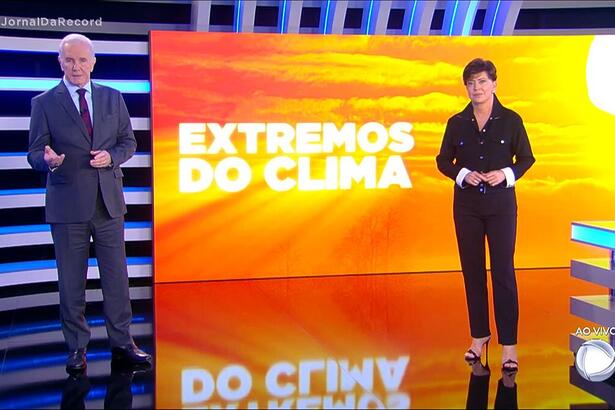 Celso Freitas e Cristina Lemos em pé no estúdio do Jornal da Record. atrás está o telão com o logo da série especial 'Extremos do Clima'