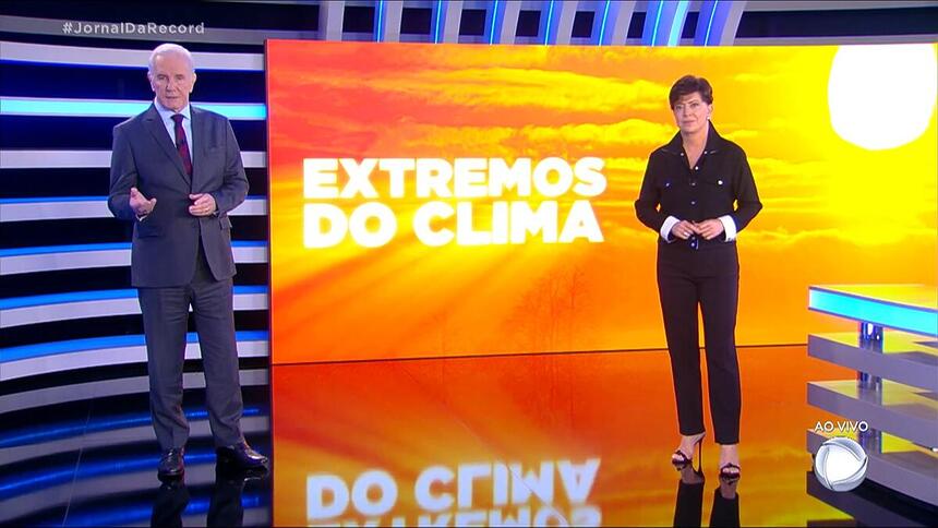 Celso Freitas e Cristina Lemos em pé no estúdio do Jornal da Record. atrás está o telão com o logo da série especial 'Extremos do Clima'