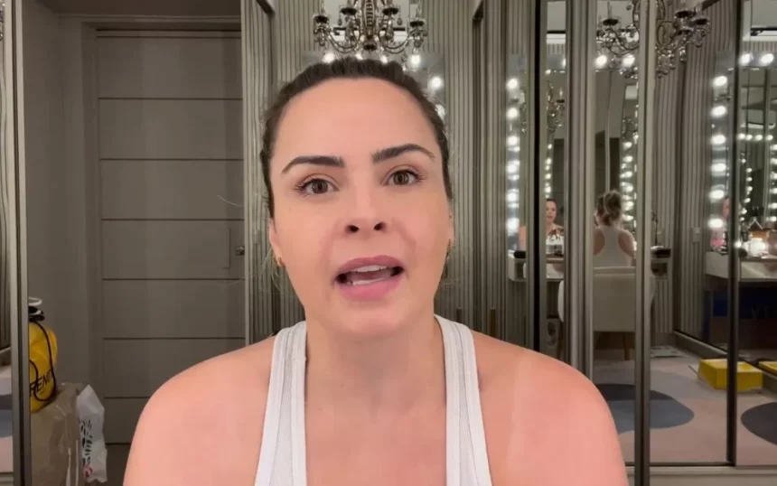 Ana Paula Renault de regata branca, gesticulando com a boca, gravando vídeo para as redes sociais sentada