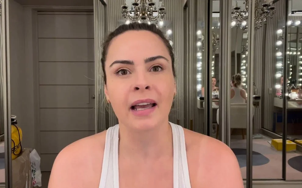 Ana Paula Renault de regata branca, gesticulando com a boca, gravando vídeo para as redes sociais sentada