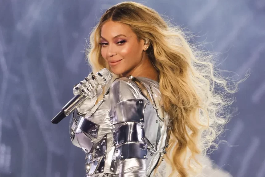 Beyoncé com look prateado, de perfil, segurando um microfone com a mão direita, durante show