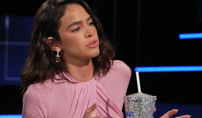 Bruna Marquezine de vestido rosa, sentada, ao lado de um copo personalizado