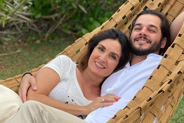 Fátima Bernades sorrindo, de camisa branca, segurando o braço de Túlio Gadelha, deitada numa rede de dormir.