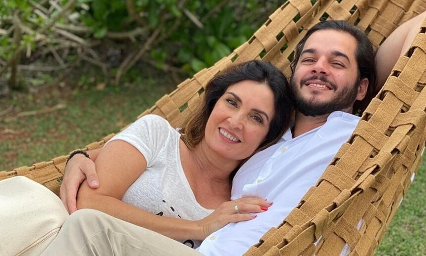 Fátima Bernades sorrindo, de camisa branca, segurando o braço de Túlio Gadelha, deitada numa rede de dormir.