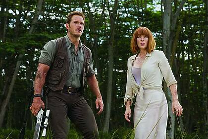 Homem com arma na mão ao lado de uma mulher assustada em cena do filme Jurassic World: O Mundo Dos Dinossauros