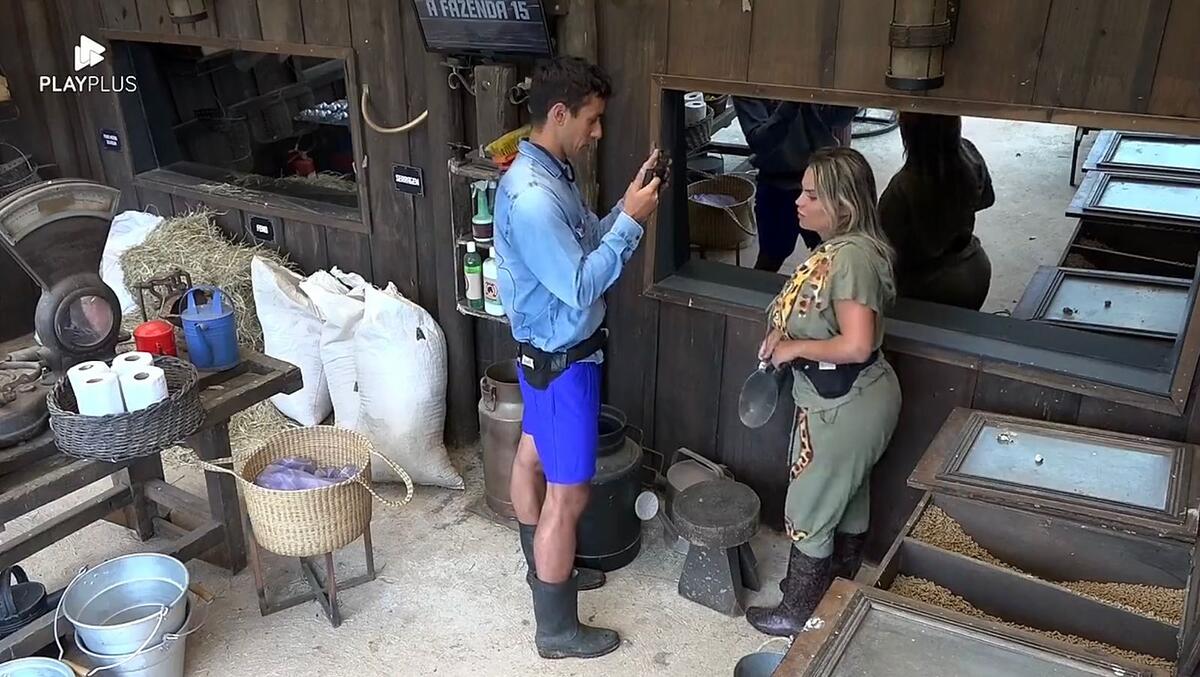 Henrique em pé, segurando o celular filmando Kally durante o trato dos animais.