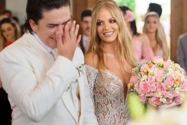 Luisa Sonza loira, de cabelo ondulado, segurando o buquê, de vestido branco, ao lado de Whindersson Nunes em seu casamento