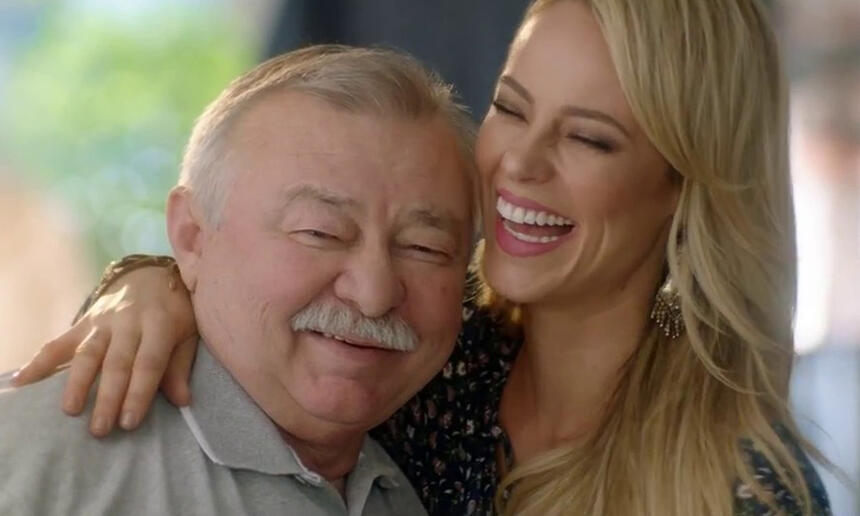 Paolla Oliveira de cabelo loiro, liso, sorrindo, abraçando o pai durante gravação de publicidade