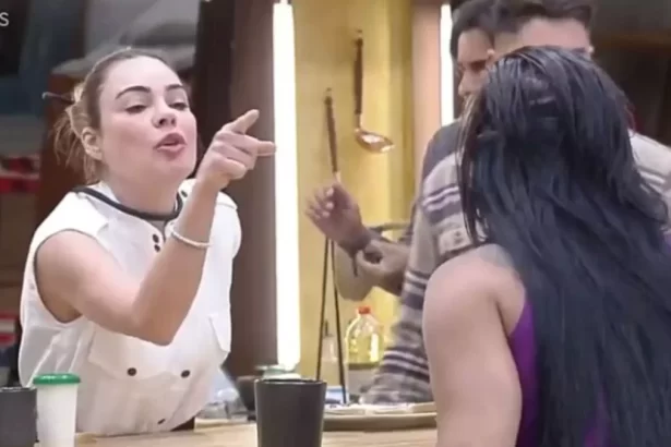 Rachel Sheherazade de camisa branca, microfone no pescoço apontando o dedo para Jenny na cozinha durante dinâmica
