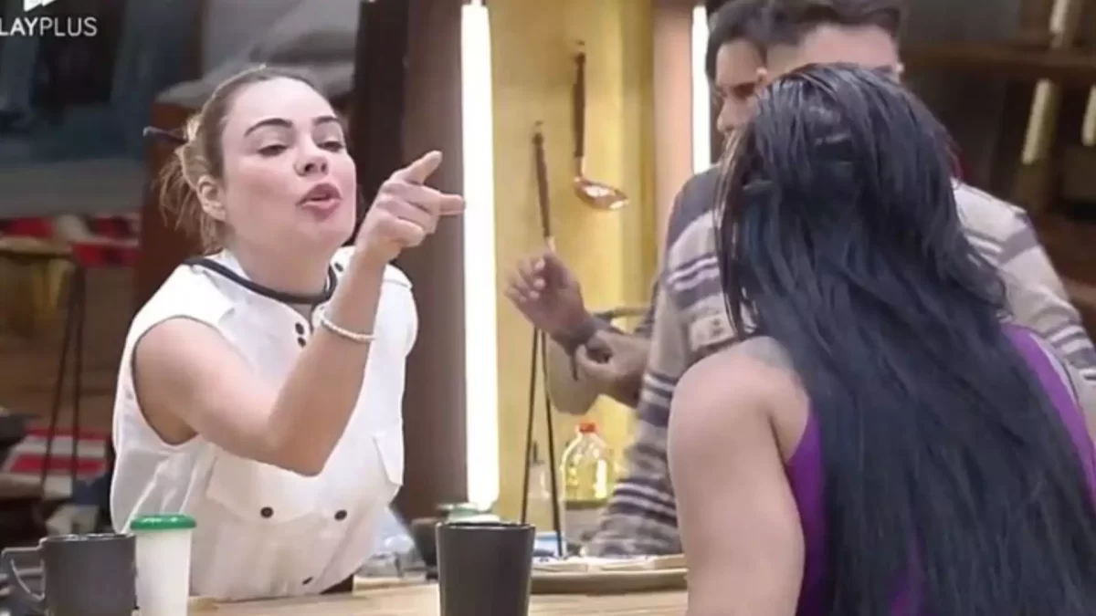 Rachel Sheherazade de camisa branca, microfone no pescoço apontando o dedo para Jenny na cozinha durante dinâmica