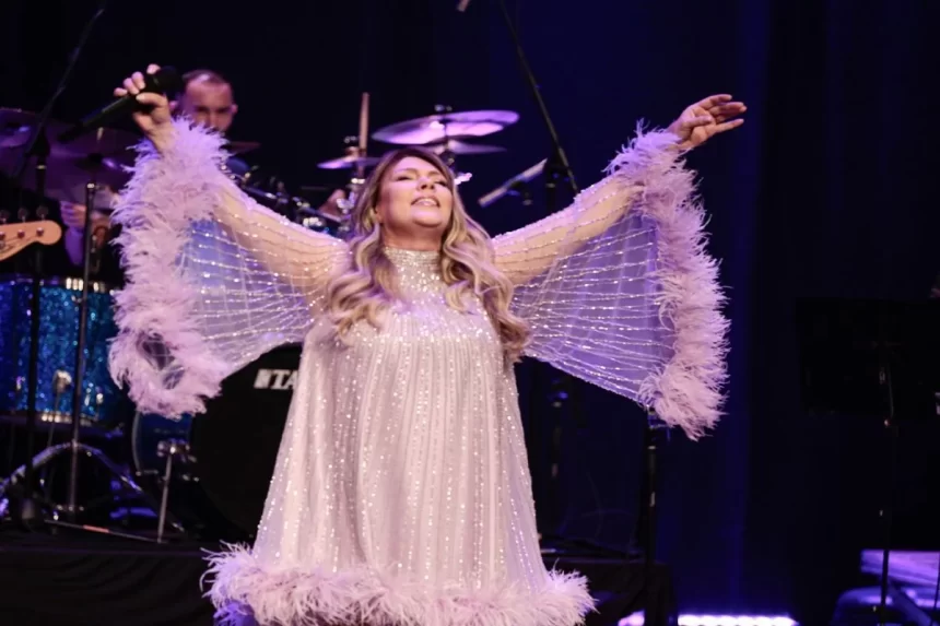 Simony de vestido roxo, com os braços abertos, segurando um microfone com a mão direita durante show