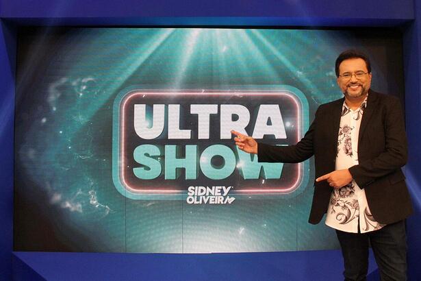 Geraldo Luís aponta para o logo do game show da RedeTV! Ultra Show