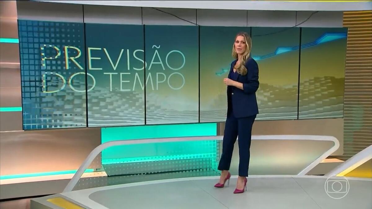 Jaqueline Brasil comandando a Previsão do Tempo com o fio caído na frente do telão