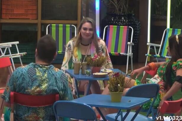 Rachel sentada na mesa de frente para Sander ao lado de Jaquelline.