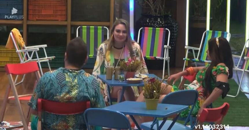 Rachel sentada na mesa de frente para Sander ao lado de Jaquelline.