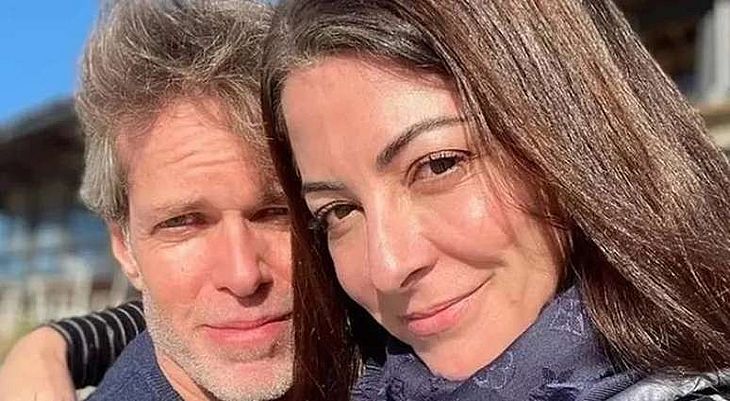 Ana Paula Padrão de cabelo solto, usando cachecol, abraçada com o marido, Gustavo Diament, durante viagem