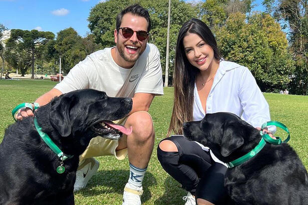 Gustavo e Lais de camisa branca, abaixados, sorrindo, ao lado dos cachorros